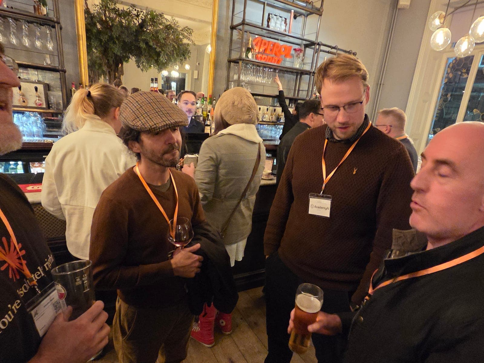Three attendees in lanyards talking over drinks in front of the bar mirror at The Lost and Found